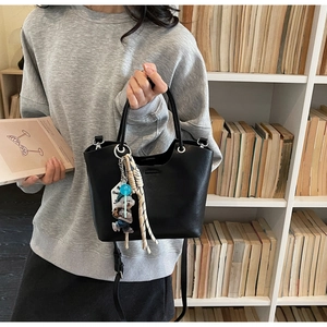 Détail du sac seau en cuir noir avec poignée argentée et breloque ours devant livres