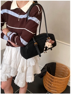 Detail of black suede baguette bag with cute puppy plush charm and gold strap hardware