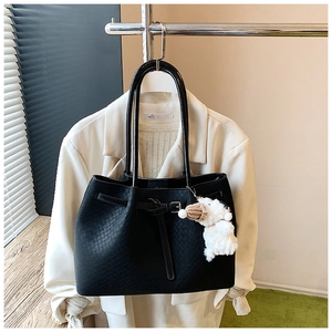 Detail of black woven tote bag with decorative strap and white plush bear pendant