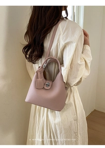Rear view of a minimalist pink-purple lychee leather bucket bag worn by a model in a studio