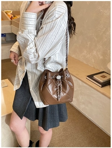Detail view of brown quilted bucket bag with chain strap on a model in a cozy cafe