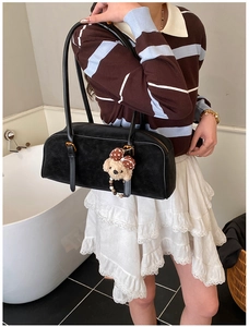 Close-up of black cylindrical shoulder bag with a cute plush bear charm on a model