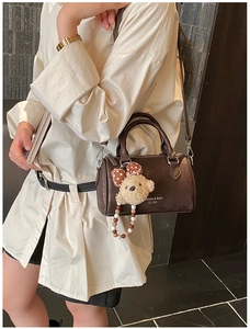 Detail of dark brown Boston bag with shoulder strap and cute teddy bear pendant charm