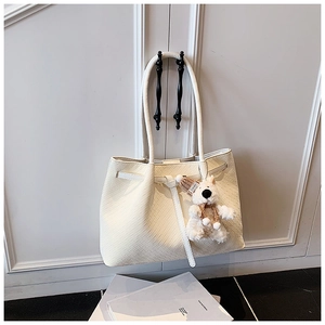 Detail of cream woven tote bag featuring checkered texture and plush bear charm
