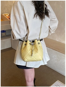 Close-up of a light yellow quilted bucket bag with chain strap worn by a model