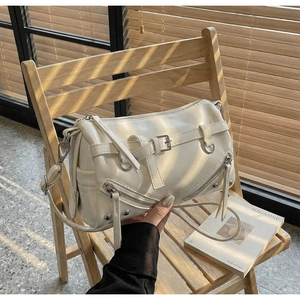 Detail view of cream bowling bag with silver studs and zippers on a wooden chair