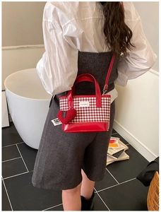 Detail of red and white checkered bucket bag with heart pendant worn by a model