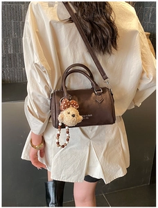Detail of dark brown leather pillow bag with plush bear charm and detachable strap