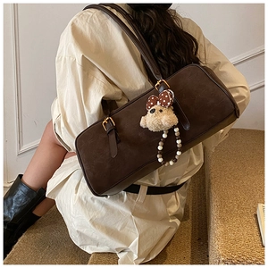 Detail of dark brown baguette bag with adjustable straps and beige plush bear charm