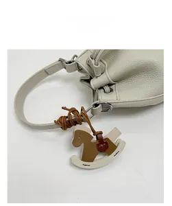 Detail of white lychee grain leather bucket bag featuring a brown horse charm pendant