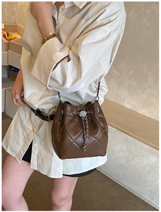 Detail of a dark brown quilted bucket bag featuring a silver metal drawstring chain strap