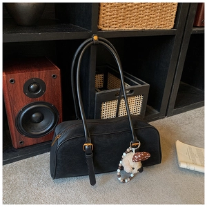 Detail of black matte suede baguette bag with cute plush puppy charm on a wooden shelf