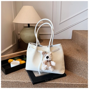 Detailed view of large white woven tote bag featuring a cute plush bear charm