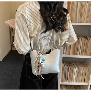 Détail du sac seau argenté métallisé avec poignées rondes en métal et breloques tendance