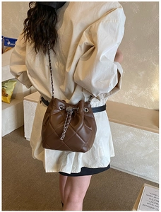 Detailed view of dark brown quilted bucket bag with chain strap worn by a model