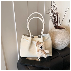 Close-up of cream woven tote bag featuring a teddy bear charm and textured weave