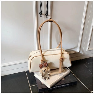 Detail of a vintage cream leather baguette bag with brown handles and a cute bear charm