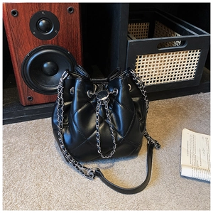 Detail of black quilted leather bucket bag with metal chain drawstring and tassel accents
