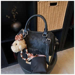 Detail of black Boston bag with leather texture, plush puppy charm and printed text