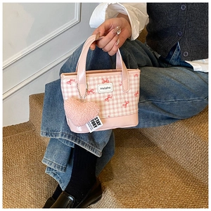 Detail of pink plaid bucket bag with red bow print and heart plush keychain accessory