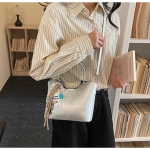 Détail du sac seau argenté avec foulard en soie, breloque ours et étiquette blanche