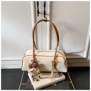 Close-up of cream rectangular shoulder bag with brown straps and cute bear pendant
