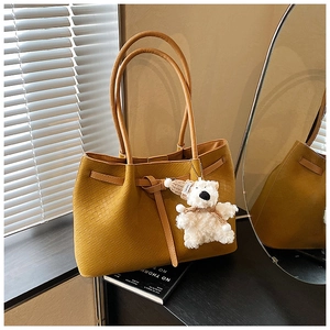 Detail of ginger woven tote bag with bow tie, teddy bear charm on black books