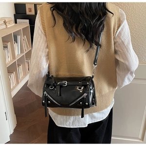 Close-up of black biker style shoulder bag with silver zippers worn over a beige vest