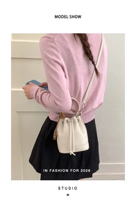 Detail view of a white drawstring bucket bag with litchi grain texture and tassel charm