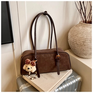 Detailed view of a vintage brown baguette bag with a plush puppy charm on a metal suitcase