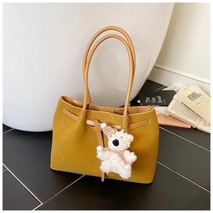 Detail of yellow woven tote bag with adjustable shoulder straps and a plush bear charm