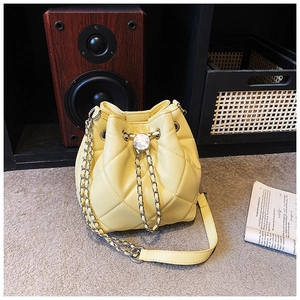Detailed close-up of yellow quilted bucket bag with silver chain and drawstring closure