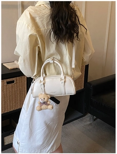 Close-up of a white Boston handbag featuring a plush bear charm and metallic texture