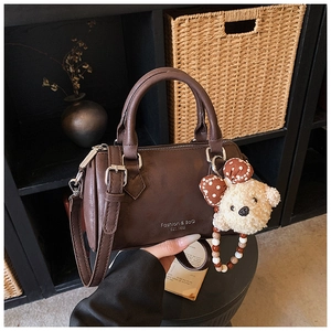 Detail view of brown Boston bag with Fashion & Bag text and cute bear charm accessory