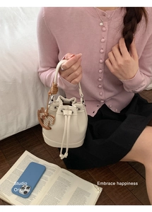 Detail view of beige lychee leather bucket bag featuring a brown wooden horse charm