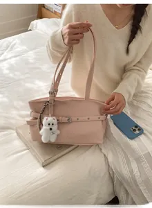 Detail view of pink tote bag with white plush puppy charm and decorative buckle straps