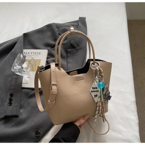 Sac seau beige élégant avec poignées et breloque dessin animé sur lit blanc