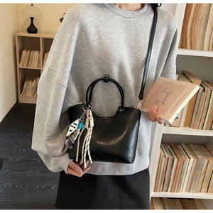Sac seau en cuir noir brillant avec breloques créatives présenté dans un intérieur cosy
