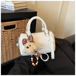 Detail of white mini boston bag with teddy bear charm and bead chain on dark suit