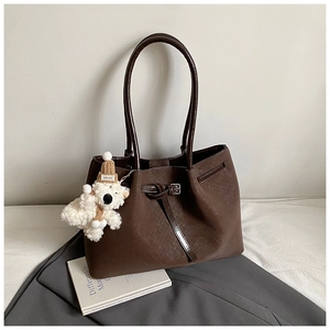 Detail of dark brown tote bag with leather buckle and white teddy bear charm accessory