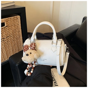 Detailed view of a white Boston bag with litchi texture, zipper, and bear charm