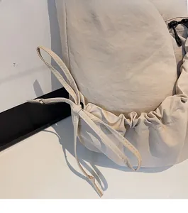 Close-up of beige dumpling bag featuring a decorative bow and drawstring pleated texture
