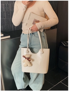 Detail of white patent leather tote bag with cute plush bear pendant and soft texture