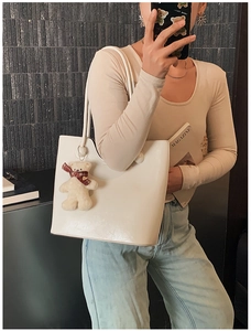 Detail of off-white glossy PU leather tote bag with a cute plush bear charm on shoulder