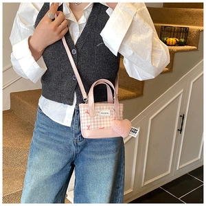 Pink checkered crossbody bucket bag with plush heart charm shown in a lifestyle setting