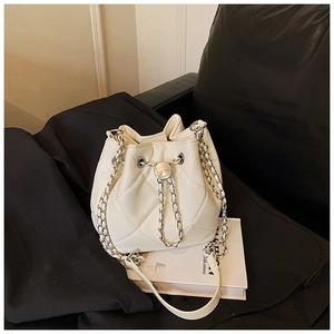 Detail of white quilted bucket bag with silver chain strap on black leather sofa