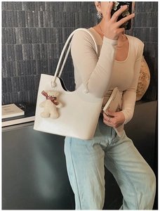 Detailed view of white glossy underarm tote bag with cute bear charm on a model