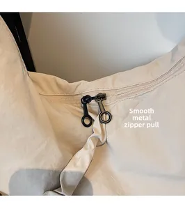 Detail of smooth black double hardware zippers on minimalist off-white nylon shoulder bag