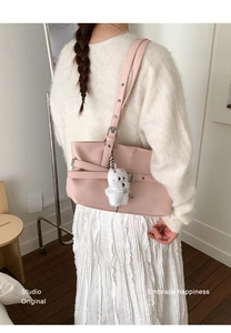 Detail of pink faux leather shoulder bag with belt buckle decor and bear charm