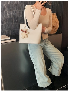 Close-up of cream leather tote bag with a cute plush bear charm on a female model